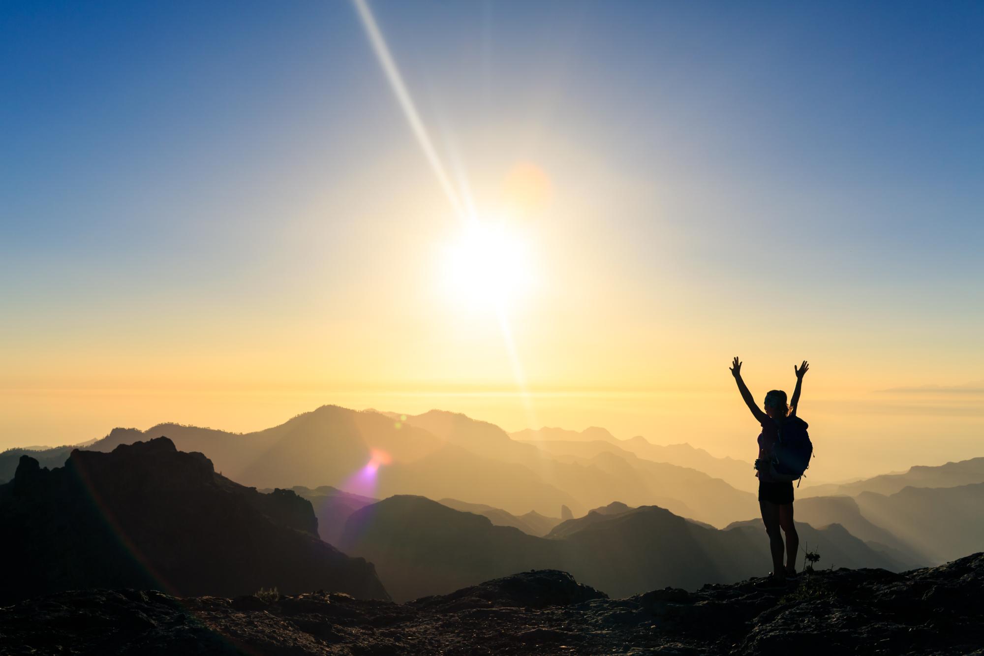 person with arms raised at mountain summit