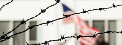 American flag on prison wall behind barbed wire.