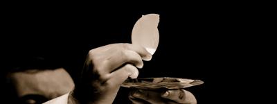 Image: hands holding the body of Christ with a black background