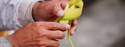 person folding cross out of palm leaf