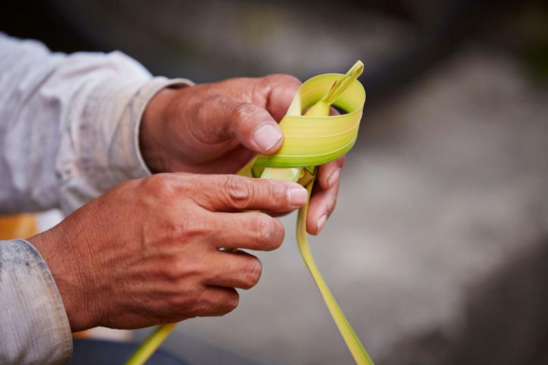 person folding cross out of palm leaf